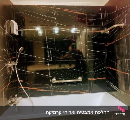 חדר אמבטיה משופץ עם אמבטיה לבנה וחיפוי קיר באריחים שחורים דמויי שיש